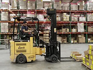 Worker operating forklift in 3PL warehouse moving boxes near shelves filled with inventory.